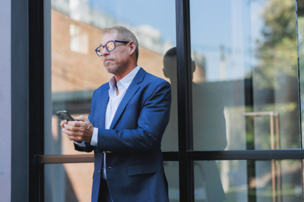 年长的商人正在查看智能手机，思考着商业策略图片下载