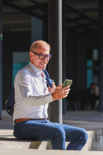 一位成熟的男士面带微笑，在户外坐着查看手机消息图片下载