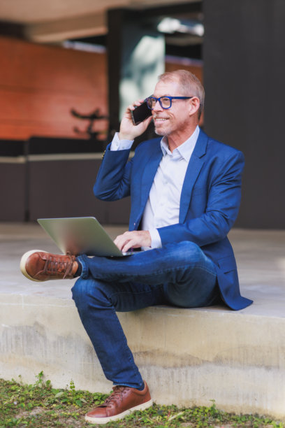 中年男子在家办公，使用笔记本电脑和手机图片下载