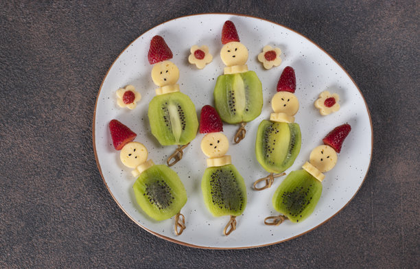 白色盘子里的奶酪、奇异果和草莓小食，摆成人物造型，背景为棕色图片下载