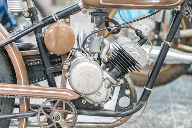 一辆棕色复古摩托车，带有银色金属部件，显露出岁月的痕迹和户外暴露的痕迹，在漫射光线下独自伫立。照片捕捉了自行车的侧面轮廓，包括图片下载