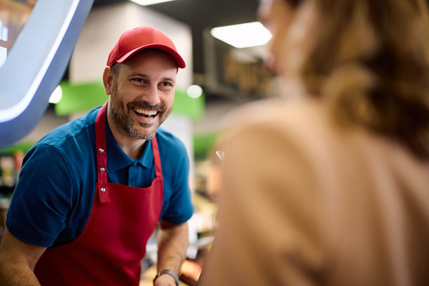 快乐的超市收银员正在与顾客交谈。图片下载