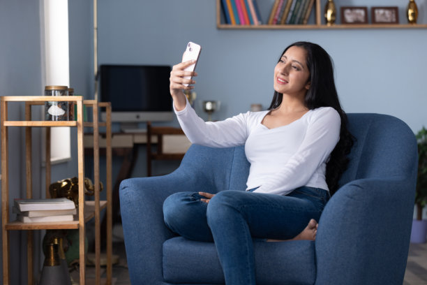 年轻女子坐在沙发上在家使用手机的素材照片图片下载