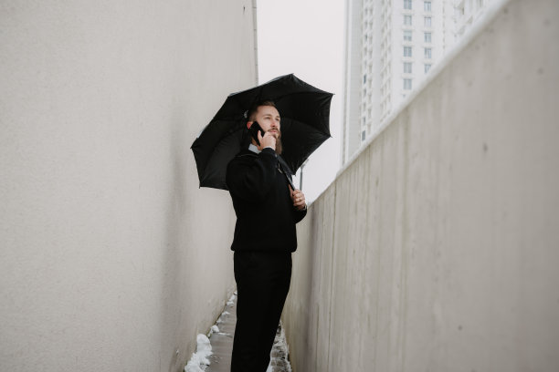 商务人士在狭窄的城市空间里撑伞接听手机图片下载