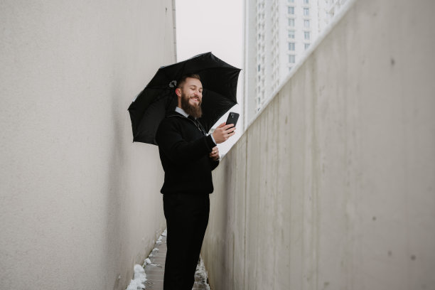 身处狭窄的城市空间，一位商务人士在雨伞下查看智能手机图片下载