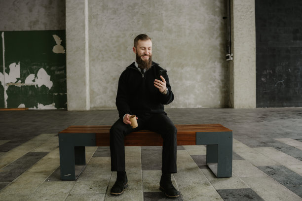 西装革履的商人坐在长椅上，在城市空间里使用智能手机，旁边放着一杯咖啡图片下载