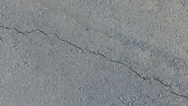 灰色沥青表面特写照片，带有细骨料。一条小裂缝斜贯画面。图片下载