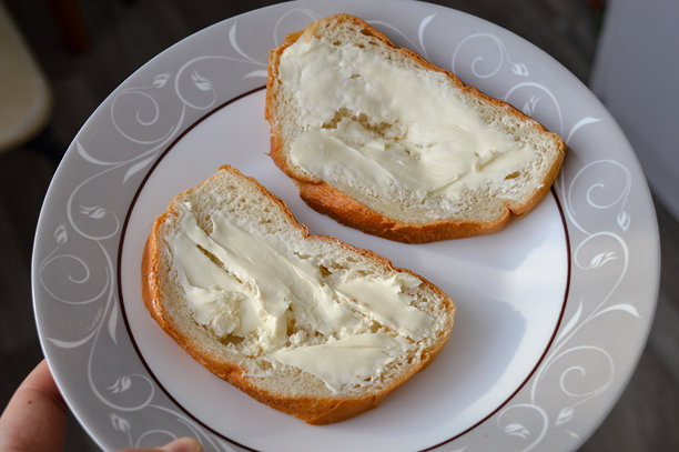 用刀将黄油涂抹在新鲜面包片上的手部特写照片。简单的自制早餐场景，自然光，日常食物准备概念。图片下载