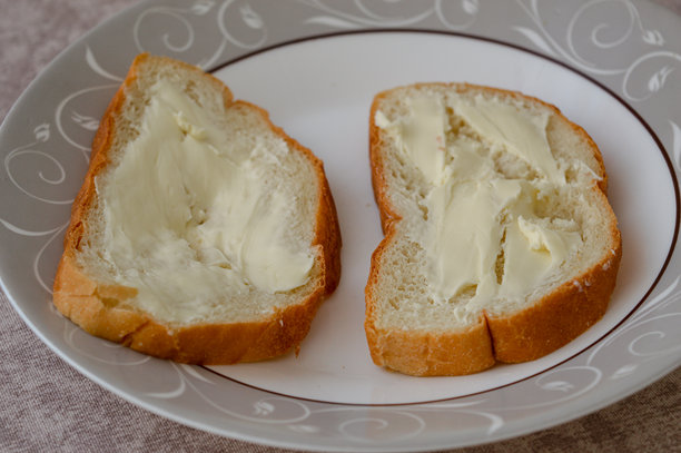 用刀将黄油涂抹在新鲜面包片上的手部特写照片。简单的自制早餐场景，自然光，日常食物准备概念。图片下载