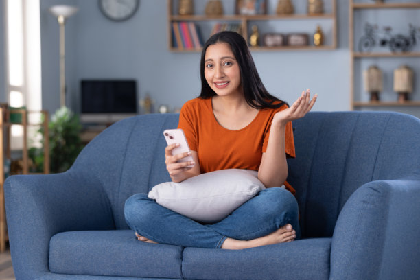 年轻貌美的女孩穿着休闲服在家里的沙发上使用手机的居家照片图片下载