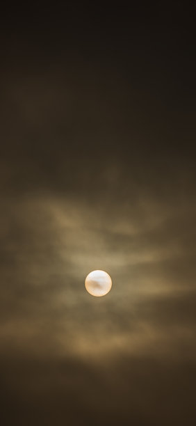 阴沉多云的天空，太阳盘被大气霾笼罩。9:19.5比例的垂直照片，展示了黑暗的自然或抽象云景。图片下载