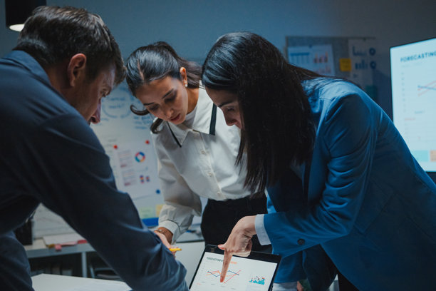 在现代办公室的夜晚，商务团队正在进行战略审查项目会议。他们在大屏幕上讨论工作流程图，旁边放着笔记本电脑。体现了团队合作、加班、战略和以截止日期为驱动的协作。图片下载