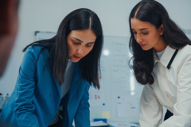 近距离拍摄的商务团队在现代办公室进行战略评审项目会议。桌上放着一台打开的笔记本电脑，大家正在讨论大屏幕上的工作流程图。体现了团队合作、战略规划和结构化协作。图片下载