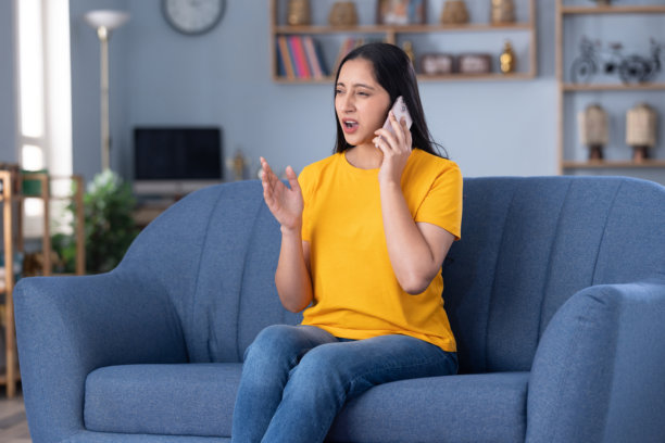 照片：一位穿着休闲服的漂亮年轻女孩在家中沙发上使用手机图片下载