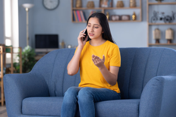 照片：一名穿着休闲服饰的漂亮年轻女孩在家中沙发上使用手机图片下载