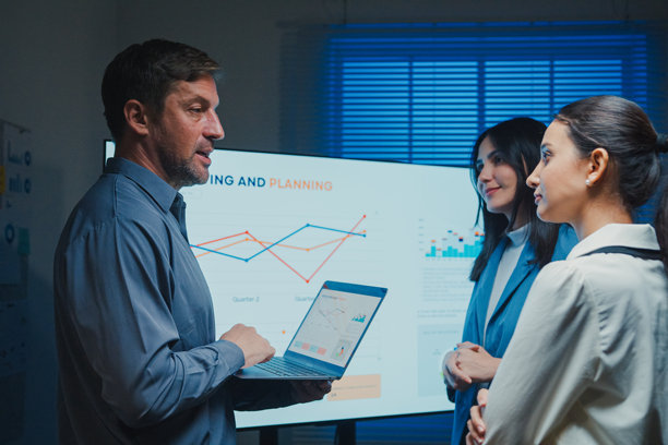 夜晚的办公室会议上，商务团队在大屏幕上展示业绩成果。团队合作、加班、沟通汇报、截止日期压力和专业决策的概念。图片下载