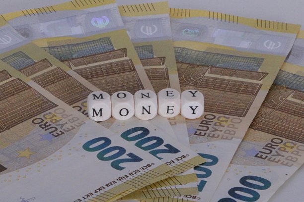 白色背景上堆叠的欧元纸币的影棚拍摄照片，纸币上方放着印有“money”字样的字母小方块。图片下载