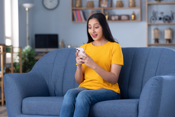 一位穿着休闲服饰的年轻漂亮女孩在家中沙发上使用手机的库存照片图片下载