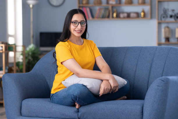 身穿休闲服饰的漂亮年轻女孩在家坐在沙发上的照片素材图片下载