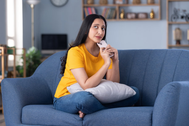 穿着休闲服装的美丽年轻女孩在家坐在沙发上玩手机的图片图片下载