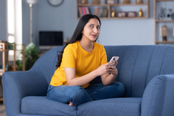 穿着休闲服的漂亮年轻女孩在家中沙发上使用手机的摄影照片图片下载