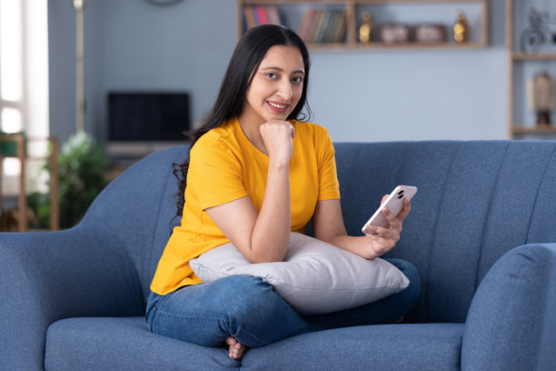 身穿休闲服的美丽年轻女子在家中沙发上使用手机的图片素材图片下载