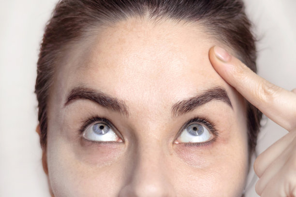 注射肉毒杆菌（Dysport）后的白人女性肖像，她用手指着自己没有皱纹的前额。手术效果显著。特写照片。图片下载