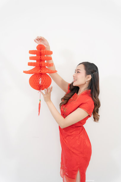 图片展示了一位美丽的亚洲女性，身着旗袍，手持中国新年装饰品红灯笼，背景为白色。图片下载