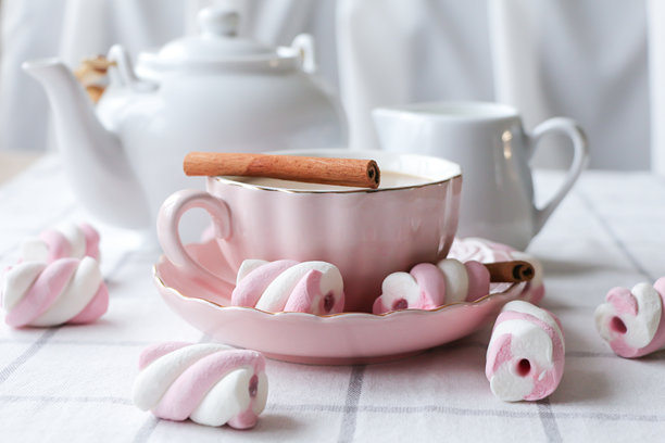 浅色桌上的粉色茶杯，里面装着奶茶、肉桂棒和棉花糖图片下载