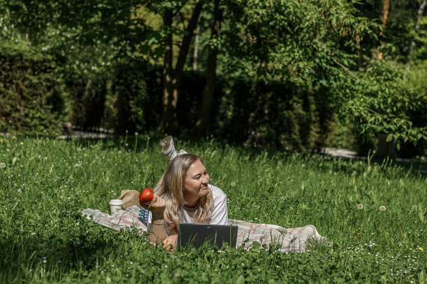 一位金发中年女子在花园的躺椅上使用笔记本电脑工作，绿色家居办公概念。图片下载