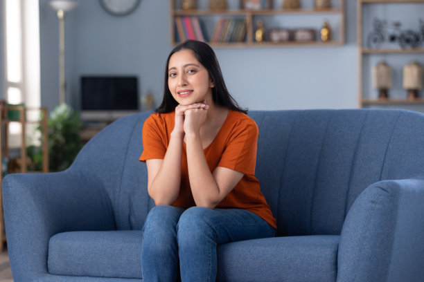 照片：穿着休闲服饰的年轻美丽女孩坐在家里的沙发上图片下载