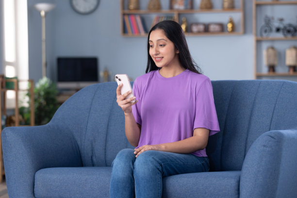 照片：一位穿着休闲服饰的漂亮年轻女孩在家中沙发上使用手机图片下载