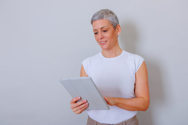 一位留着灰色短发的成熟的女士，微笑着使用现代数字技术，手持平板电脑并滑动屏幕。图片下载