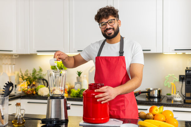 阿拉伯年轻男子在厨房的搅拌机中加入乳清蛋白粉制作健身后冰沙图片下载