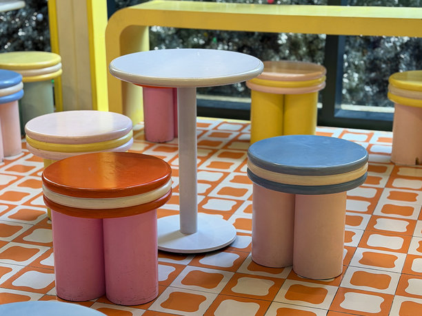 充满活力的区域，有色彩鲜艳的复古图案桌子、凳子和椅子，配有 pedestal 桌和长凳座椅。图片下载