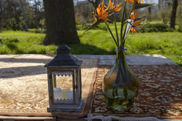 绿色玻璃瓶中的天堂鸟花和公园地毯上的复古灯笼图片下载