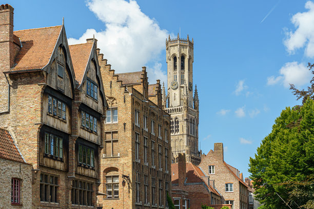 比利时布鲁日城市中一排红砖老房子和一个高耸的哥特式钟楼。照片是从运河水面上拍摄的。图片下载