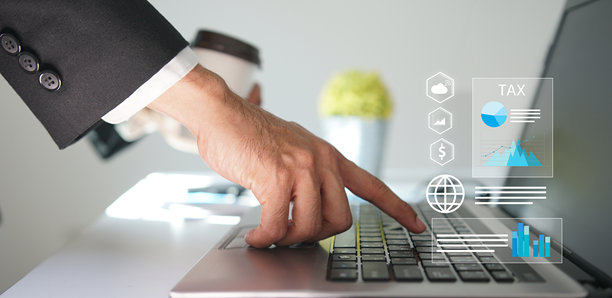 商人的手正在操作一台笔记本电脑，电脑屏幕上显示着税收相关的图标和财务图表的虚拟现实界面，代表着税务规划和财务管理。图片下载