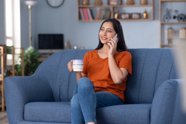 年轻漂亮的女孩在家坐在沙发上玩手机的居家照片图片下载