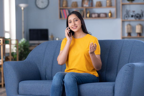 照片：一位漂亮的年轻女孩在家坐在沙发上使用手机图片下载