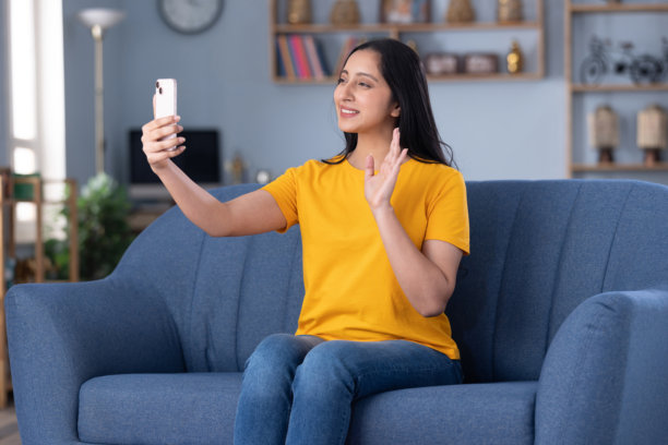 照片：一位年轻美丽的女孩在家中坐在沙发上使用手机图片下载