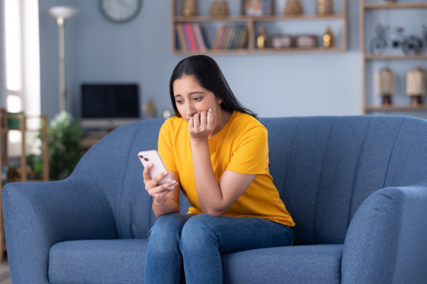 一名年轻美丽的女孩在家中坐在沙发上使用手机的图片图片下载