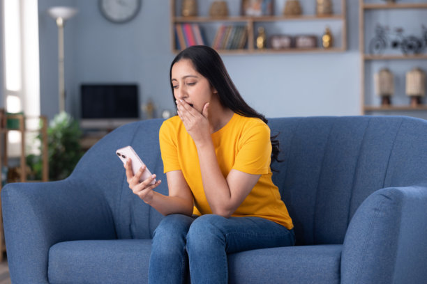 漂亮的年轻女孩在家中坐在沙发上使用手机的图片素材图片下载