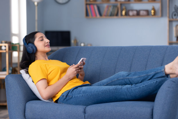 美丽的年轻女孩在家中坐在沙发上听音乐的图片素材图片下载