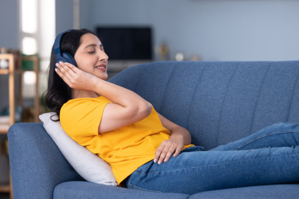 照片：一位美丽的年轻女孩在家坐在沙发上听音乐图片下载