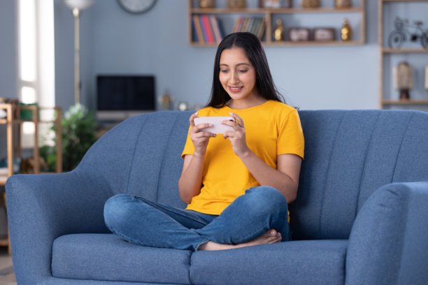 年轻漂亮的女孩在家坐在沙发上玩手机的图片图片下载