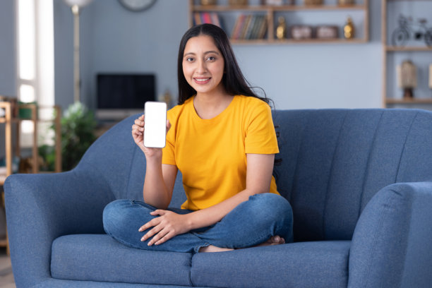 照片：一位美丽的年轻女子在家中的沙发上坐着，展示着设备屏幕图片下载