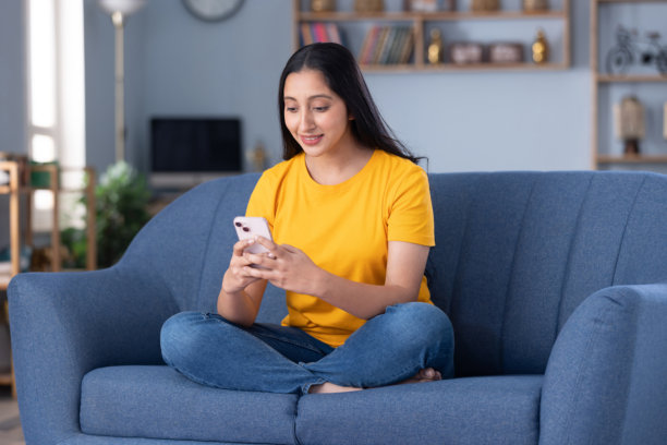 年轻美丽的女孩在家中坐在沙发上使用手机的图片图片下载