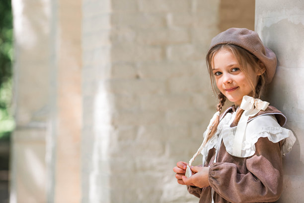 一位小女孩，头发上系着蝴蝶结，身穿米色连衣裙，头戴贝雷帽，在户外。复古女式配饰和复古风格服装。图片下载