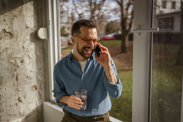 一个男人在室内靠窗处开心地笑着打电话图片下载